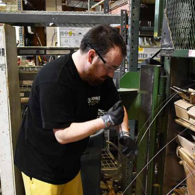 Jesse threads steel bands through the compacted stack of cardboard he’s broken down. When the cardboard is compressed a final time, the compactor will draw the steel bands tight around the bundle.